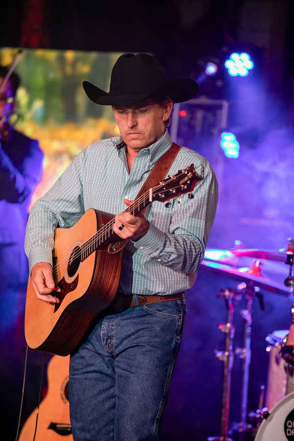 Male lead tribute performing playing guitar intently onstage in cowboy hat and blue button up shirt during his tribute to George Strait | Altus Entertainment